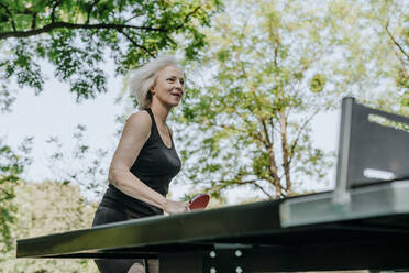Lächelnde reife Frau spielt Tischtennis im Park - YTF00060