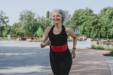 Glückliche reife Frau mit Hosenbund beim Joggen im Park - YTF00062