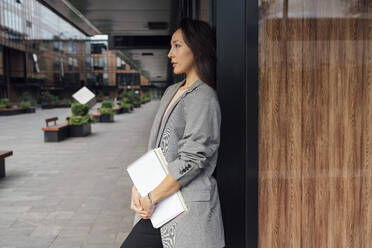 Businesswoman with documents standing outside office building - VPIF07119