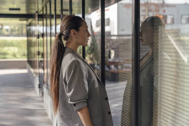 Geschäftsfrau mit langen Haaren betrachtet Spiegelung auf Glaswand - VPIF07151