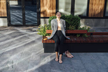 Smiling thoughtful businesswoman sitting on bench at office park - VPIF07155