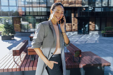 Happy businesswoman with hand in pocket talking on mobile phone - VPIF07172