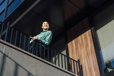 Lächelnde Geschäftsfrau genießt den sonnigen Tag und lehnt sich an ein Geländer - VPIF07191
