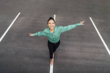 Happy businesswoman with arms outstretched balancing on road marking - VPIF07196