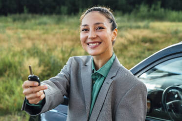 Happy beautiful saleswoman with key standing in front of car - VPIF07206