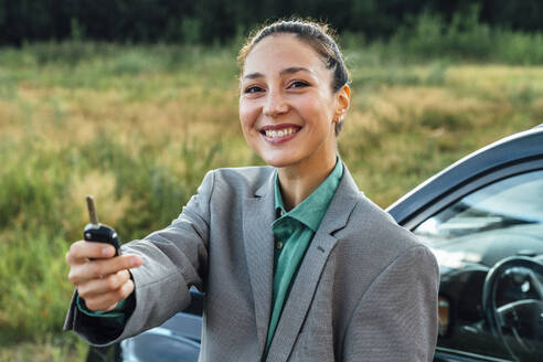 Glückliche schöne Verkäuferin mit Schlüssel vor einem Auto stehend - VPIF07206