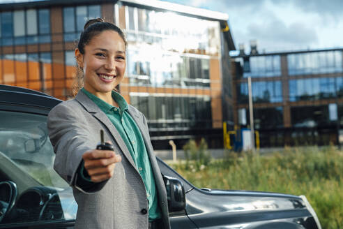 Geschäftsfrau mit Schlüssel und Auto vor einem Bürogebäude an einem sonnigen Tag - VPIF07207