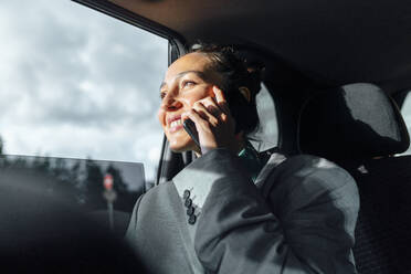 Glückliche Geschäftsfrau, die im Auto sitzend mit ihrem Smartphone spricht - VPIF07209