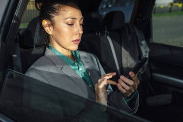 Geschäftsfrau, die im Auto sitzend eine Textnachricht über ihr Smartphone verschickt - VPIF07210