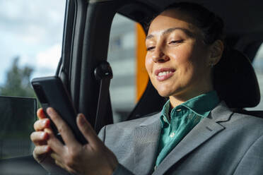 Lächelnde Geschäftsfrau, die im Auto mit ihrem Mobiltelefon im Internet surft - VPIF07212