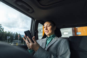 Glückliche Geschäftsfrau, die im Auto sitzend ein Smartphone benutzt - VPIF07213