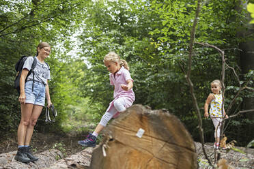 Smiling mother looking at daughter moving down from tree trunk - DWF00597