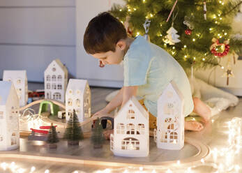 Junge spielt mit Spielzeugeisenbahn in der Nähe des Weihnachtsbaums zu Hause - ONAF00101