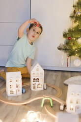 Süßer Junge spielt mit Miniatur-Eisenbahn Spielzeug in der Nähe von Weihnachtsbaum zu Hause - ONAF00103