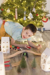 Glücklicher Junge spielt mit Miniatur-Spielzeugeisenbahn unter dem Weihnachtsbaum zu Hause - ONAF00106