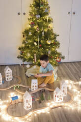 Junge spielt mit Holzeisenbahn in der Nähe von Weihnachtsbaumschmuck zu Hause - ONAF00113