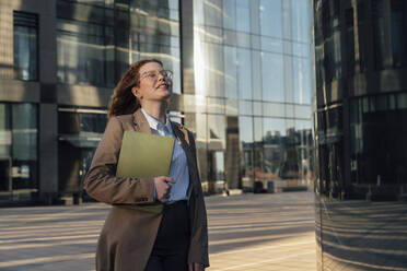 Smiling businesswoman with eyes closed standing by office building - VPIF07227