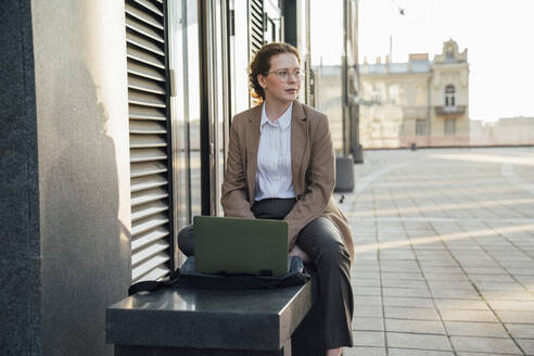 Nachdenklicher junger Freiberufler mit Laptop auf einer Bank sitzend - VPIF07245