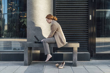 Young redhead freelancer using laptop by office building - VPIF07248