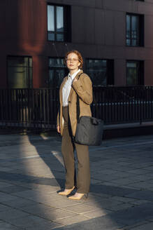 Junge Geschäftsfrau mit Laptoptasche auf dem Fußweg stehend - VPIF07254