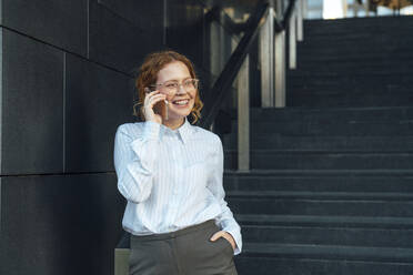 Lächelnde Geschäftsfrau, die an der Treppe mit ihrem Handy telefoniert - VPIF07269