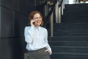 Smiling businesswoman talking on mobile phone by staircase - VPIF07269