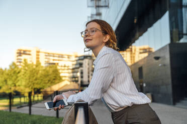 Lächelnde Geschäftsfrau mit Smartphone, die sich auf ein Geländer stützt - VPIF07276