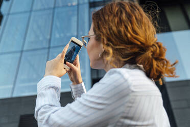 Businesswoman photographing office building through mobile phone - VPIF07278