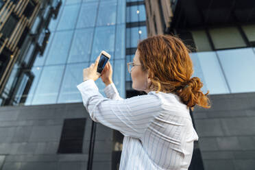 Junge Geschäftsfrau fotografiert Gebäude mit dem Mobiltelefon - VPIF07279