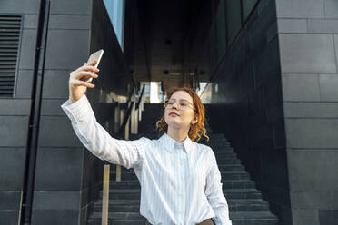 Young businesswoman with eyeglasses taking selfie through smart phone - VPIF07280