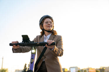 Lächelnde Geschäftsfrau mit Helm, die einen elektrischen Motorroller fährt - VPIF07291