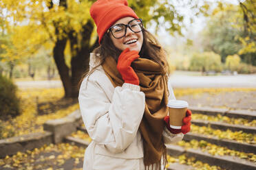 Smiling woman holding disposable cup enjoying at park - OYF00748