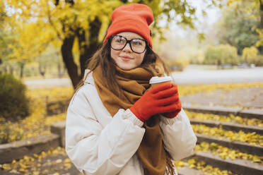 Thoughtful smiling woman holding disposable cup at park - OYF00749