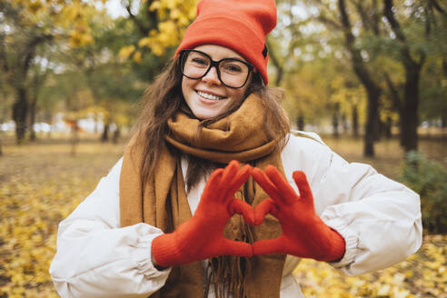 Lächelnde junge Frau gestikuliert Herzform im Park - OYF00752