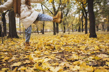 Woman kicking autumn leaves at park - OYF00764