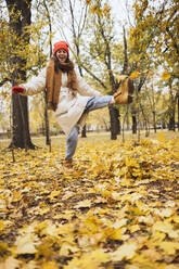 Glückliche junge Frau, die im Park gegen Herbstblätter tritt - OYF00765
