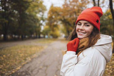 Smiling woman wearing warm clothing enjoying at park - OYF00771