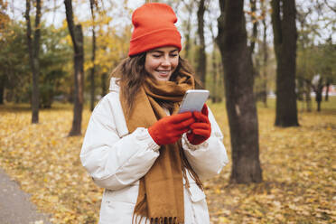 Smiling woman using smart phone in autumn park - OYF00774
