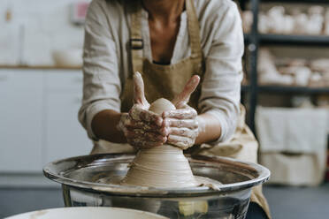 Hände einer Handwerkerin beim Formen von Ton auf einer Töpferscheibe in einer Werkstatt - YTF00068