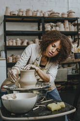 Young craftswoman molding pot shape on pottery wheel - YTF00072