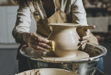 Hands of potter molding pot shape on pottery wheel - YTF00074