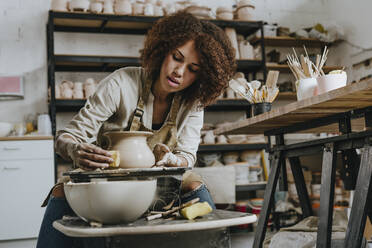 Young potter molding pot shape on pottery wheel at workshop - YTF00075