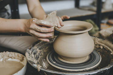 Hands of potter molding pot on pottery wheel at workshop - YTF00078