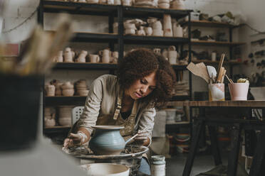 Young potter painting pot on pottery wheel at workshop - YTF00080