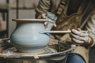 Hand's of potter painting pot on pottery wheel at workshop - YTF00081