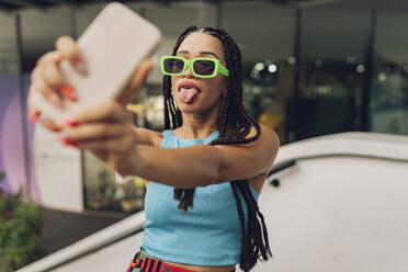 Frau streckt ihre Zunge heraus und macht ein Selfie mit ihrem Smartphone - JCCMF07288