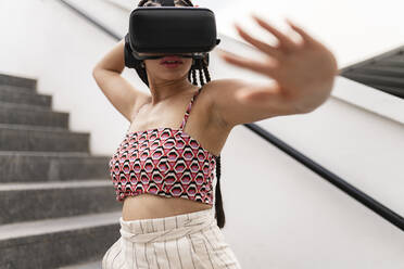Frau mit Virtual-Reality-Simulator gestikuliert auf einer Treppe - JCCMF07317