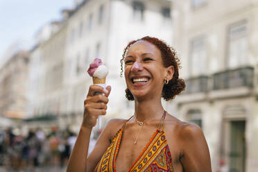 Fröhliche junge Frau mit lockigem Haar genießt Eiscreme - DCRF01409