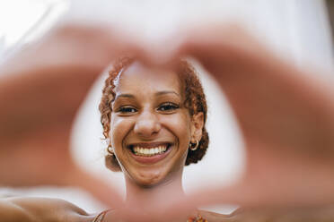 Happy young woman looking through heart shape made of hands - DCRF01417