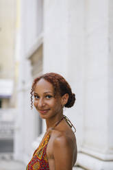 Smiling woman with curly hair standing in front of building - DCRF01421